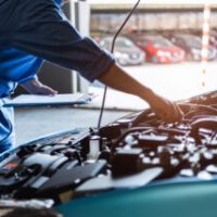 Car mechanic holding clipboard and checking to maintenance vehicle by customer claim order in auto repair shop garage. engine repair service. people occupation and business job. automobile technician